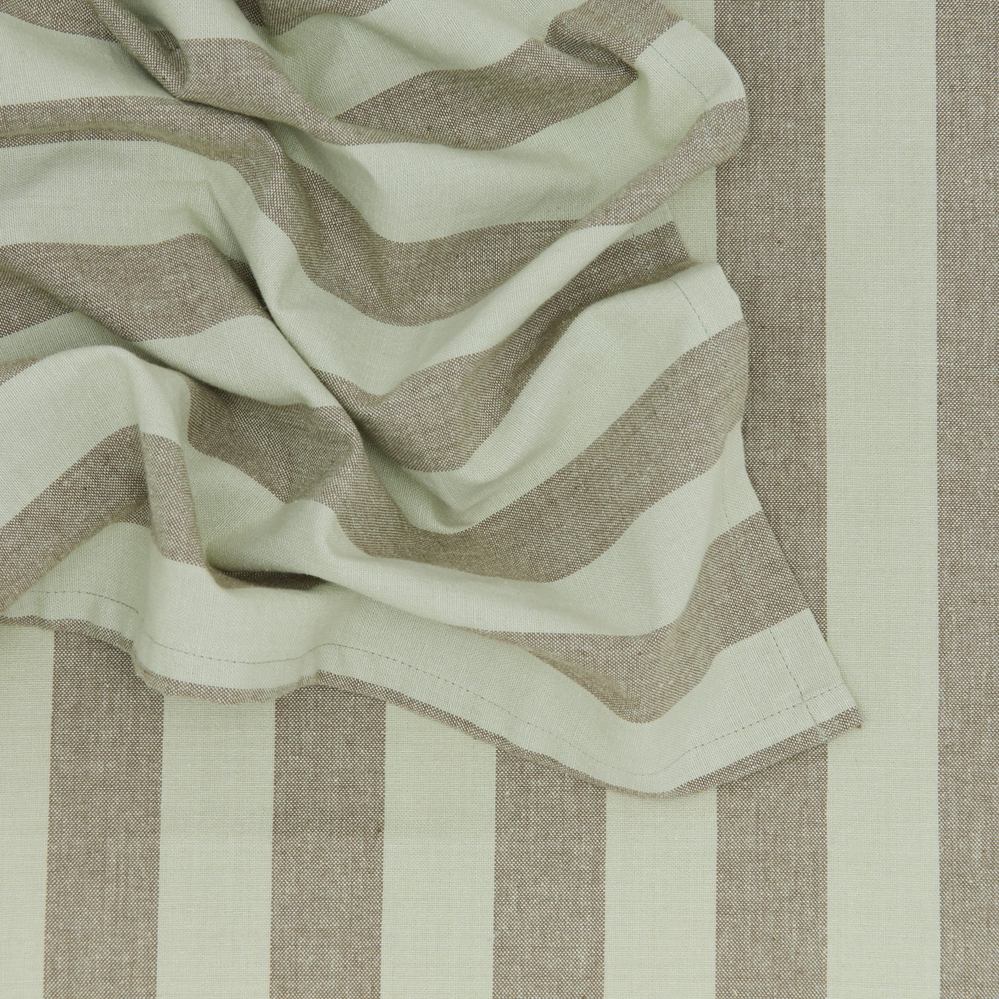Close-up of crumpled Essential Striped Placemats (Set of 4) by Hawkins New York, featuring thick green and beige stripes against a matching striped backdrop, conveying an effortless sense of easy living.