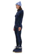 A person stands facing left, wearing a blue beanie, a dark blue midweight blend long-sleeve top, matching Halfdays Hallie Merino Legging with blue lines, and black and white boots.