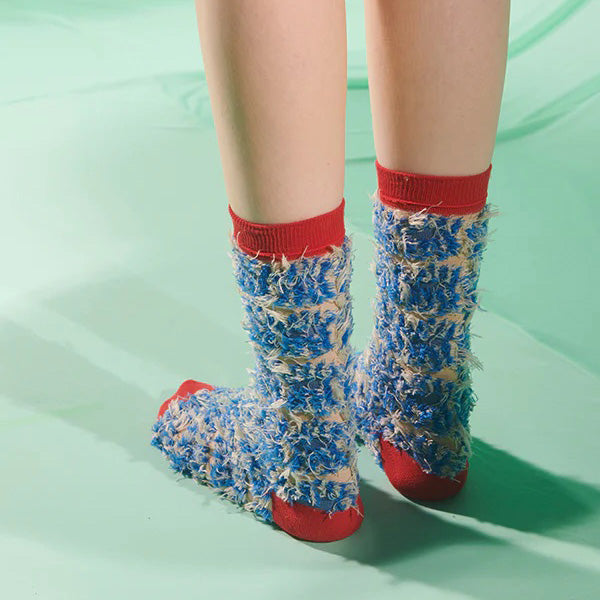 Someone wears Henrik Vibskov's Hairy Handsome Chair Socks Femme in red, textured with blue and beige abstract yarn, while standing on a light green surface.