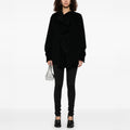 A person in a black oversized jacket and Henrik Vibskov's Honey Leggings, featuring an elastic waistband, holds a small silver handbag against a plain white background.