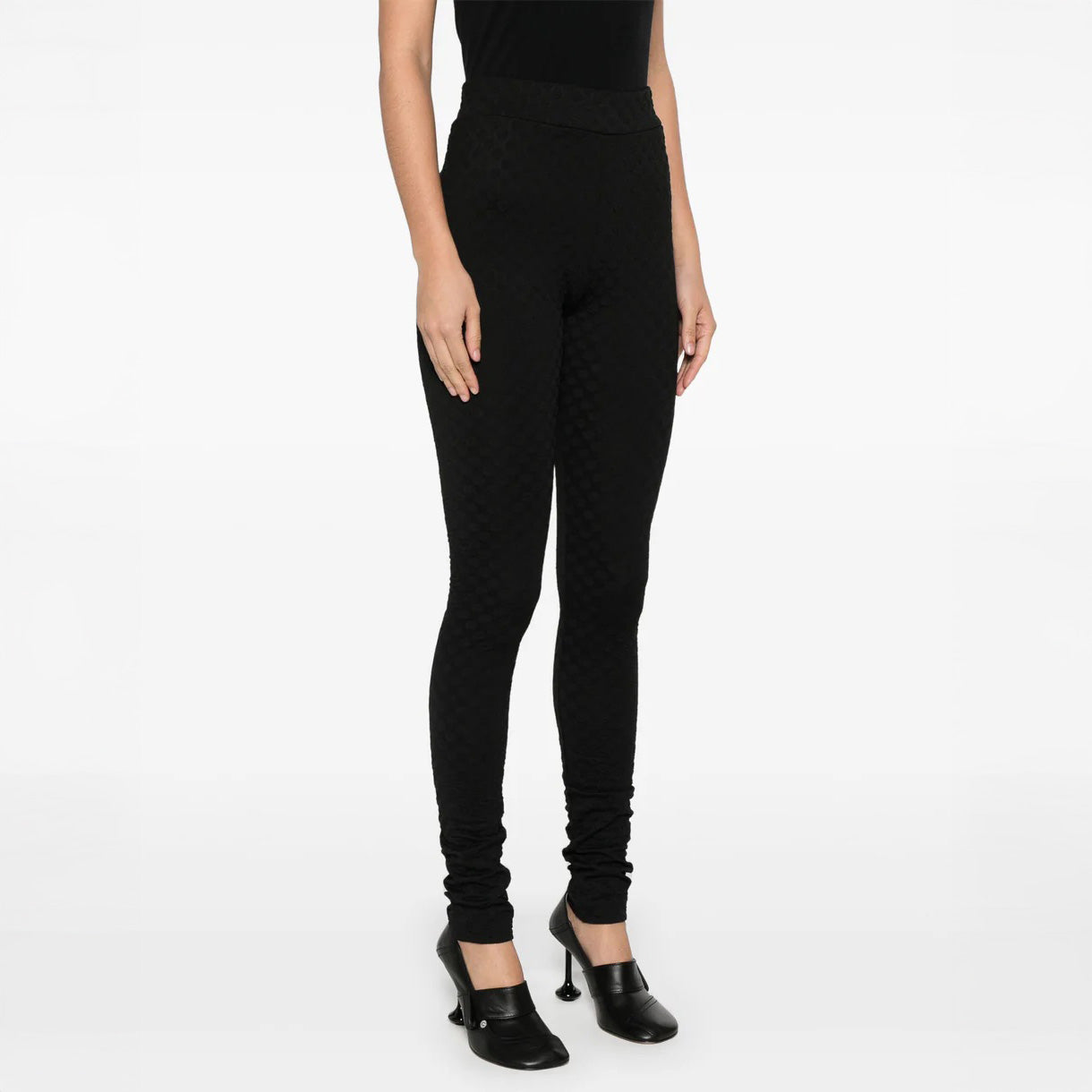Person in Henrik Vibskov's Honey Leggings, featuring a textured black design and elastic waistband, paired with black shoes against a white backdrop. Upper body is partially visible.
