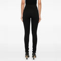 A person wearing Honey Leggings by Henrik Vibskov, featuring a high-waisted elastic waistband and textured design, stands in black heels against a plain background, back view shown.