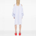 A person stands with back to camera in a loose light blue New Bumble Shirtdress by Henrik Vibskov, featuring shoulder cutouts, paired with bright red platform shoes against a plain white background.