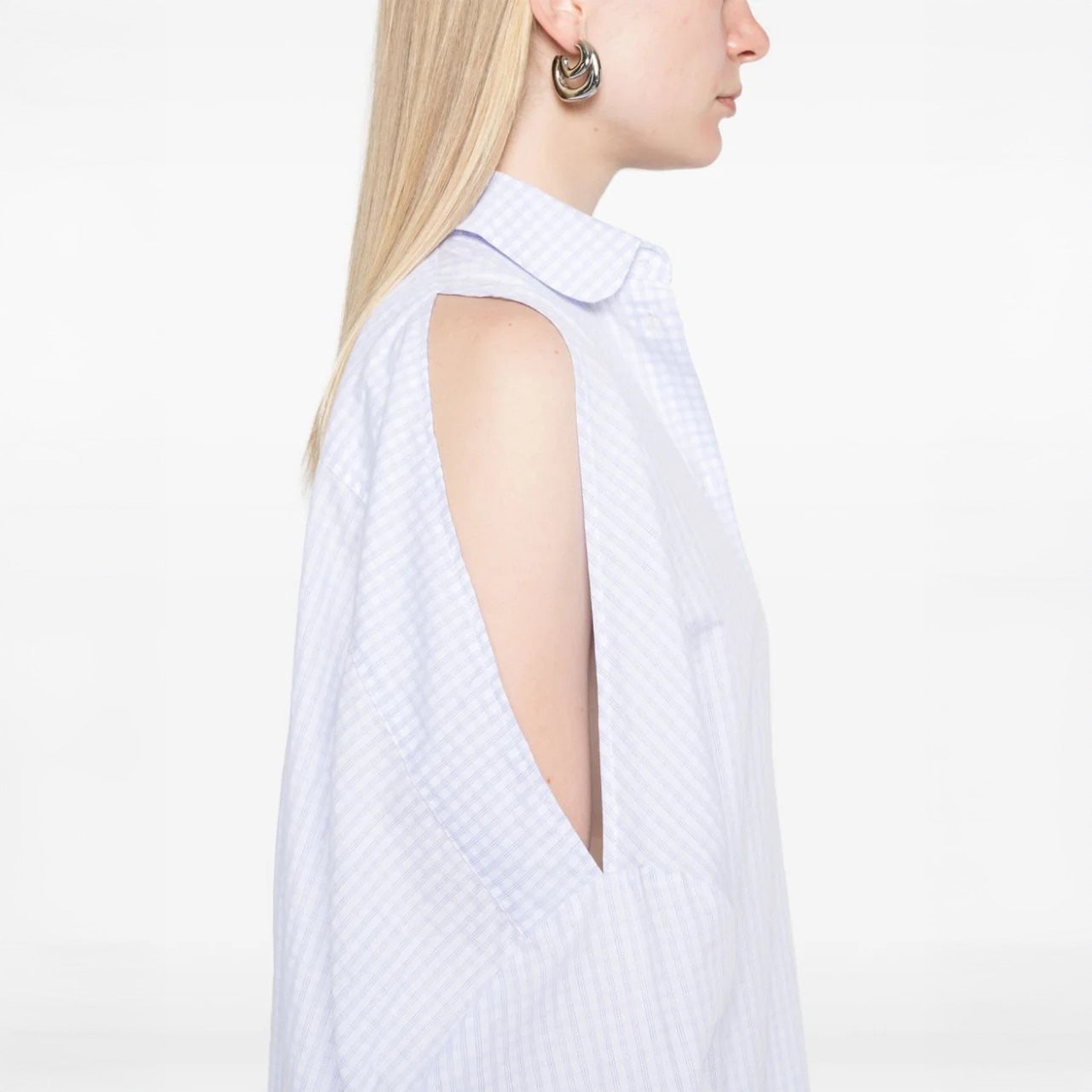 A woman in profile wears the Henrik Vibskov New Bumble Shirtdress with open shoulder slits and gold hoop earrings, set against a plain white background.