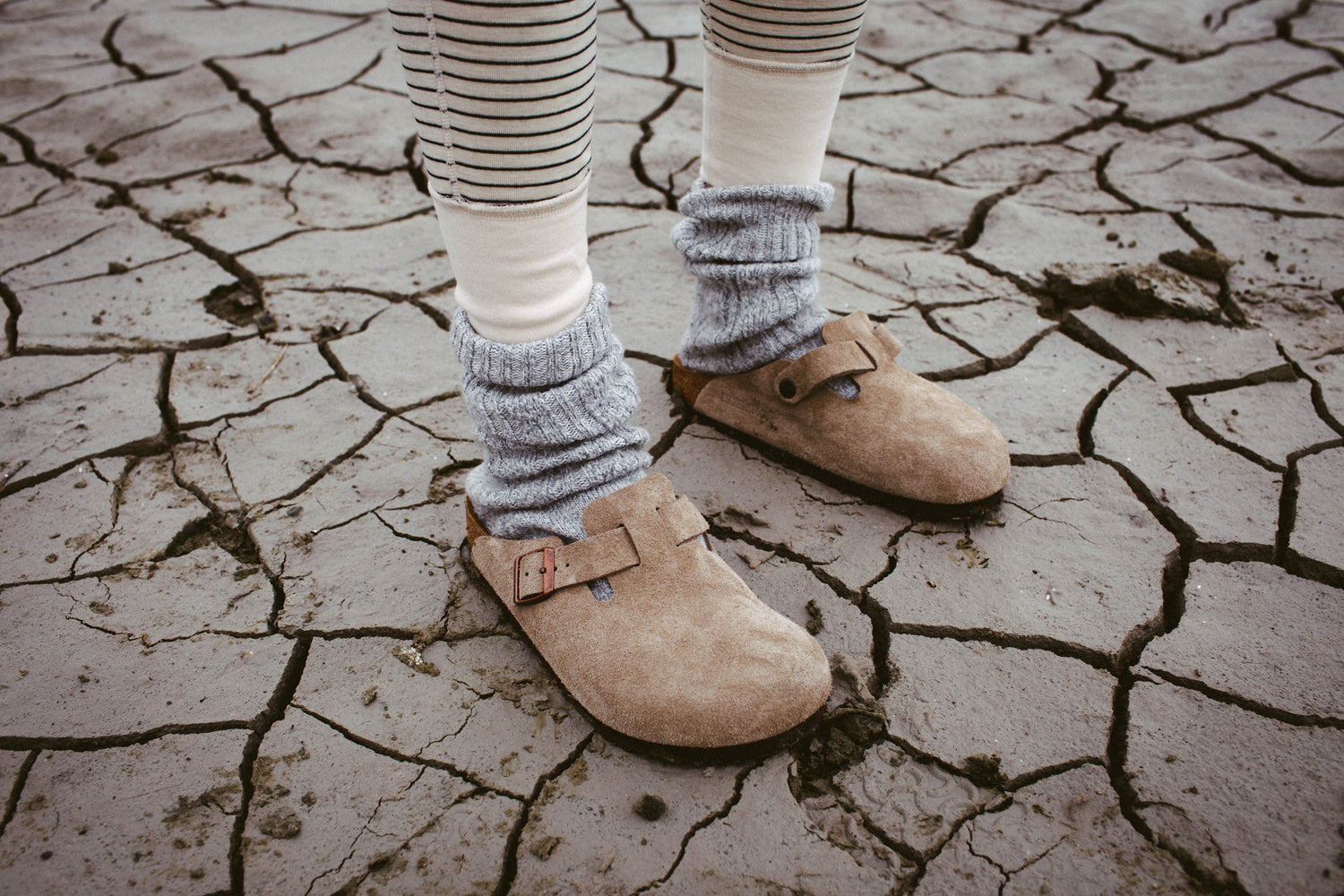 legs in black beige striped leggins and grey socks wearing birkenstocks on dried clay 