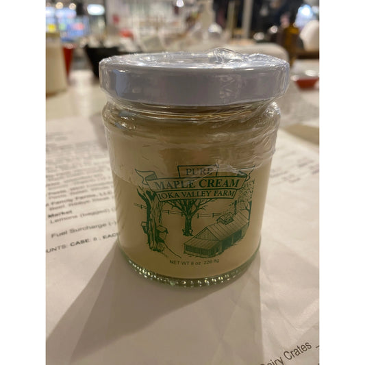 A jar of Westerlind Maple Cream from Oka Valley Farm, sealed with a white cap, displayed on a table with blurred background.