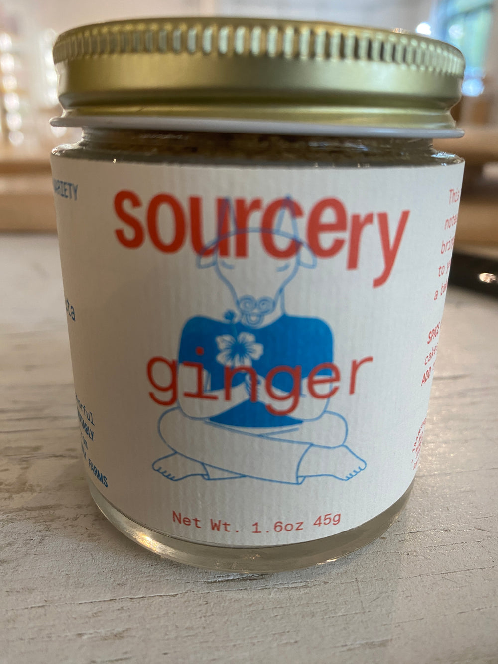 A 1.6 oz (45g) jar marked "Sourcery Ginger" by Westerlind, adorned with a gold lid and a design of a seated figure holding flowers.