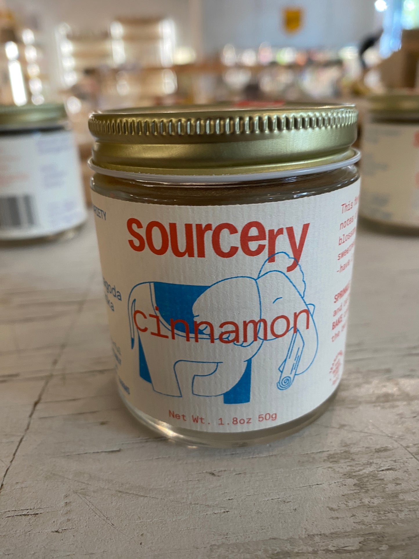 A jar of "Sourcery Cinnamon" by Westerlind, featuring an elephant logo, rests on a wooden surface.