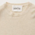 The Inga Sweater by Aiayu is a beige cashmere piece with classic ribbed edges and a label displaying the brand name.