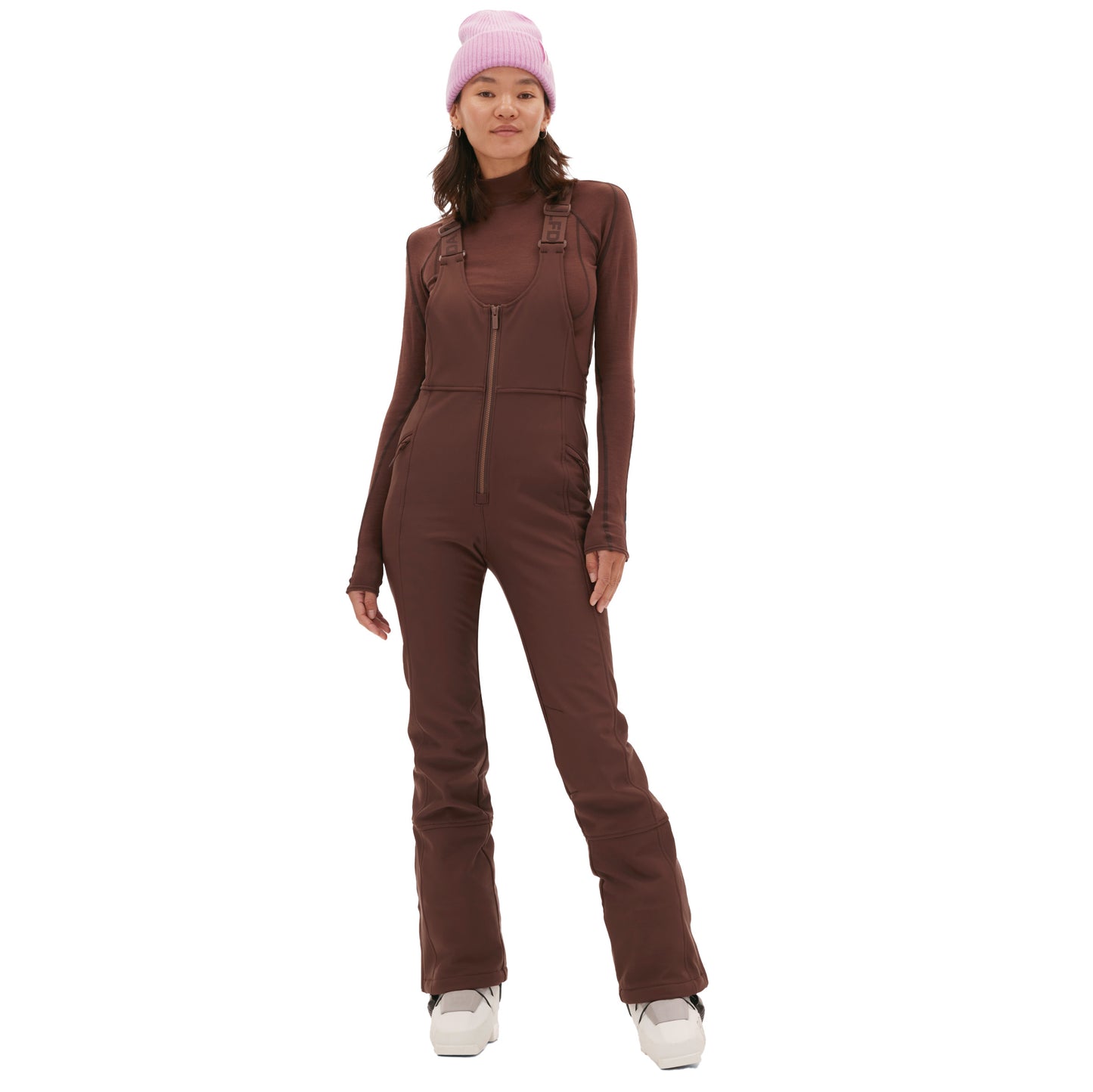 A person in an Isabel Soft Shell Bib Pant by Halfdays, a pink beanie, and white shoes stands against a white background.