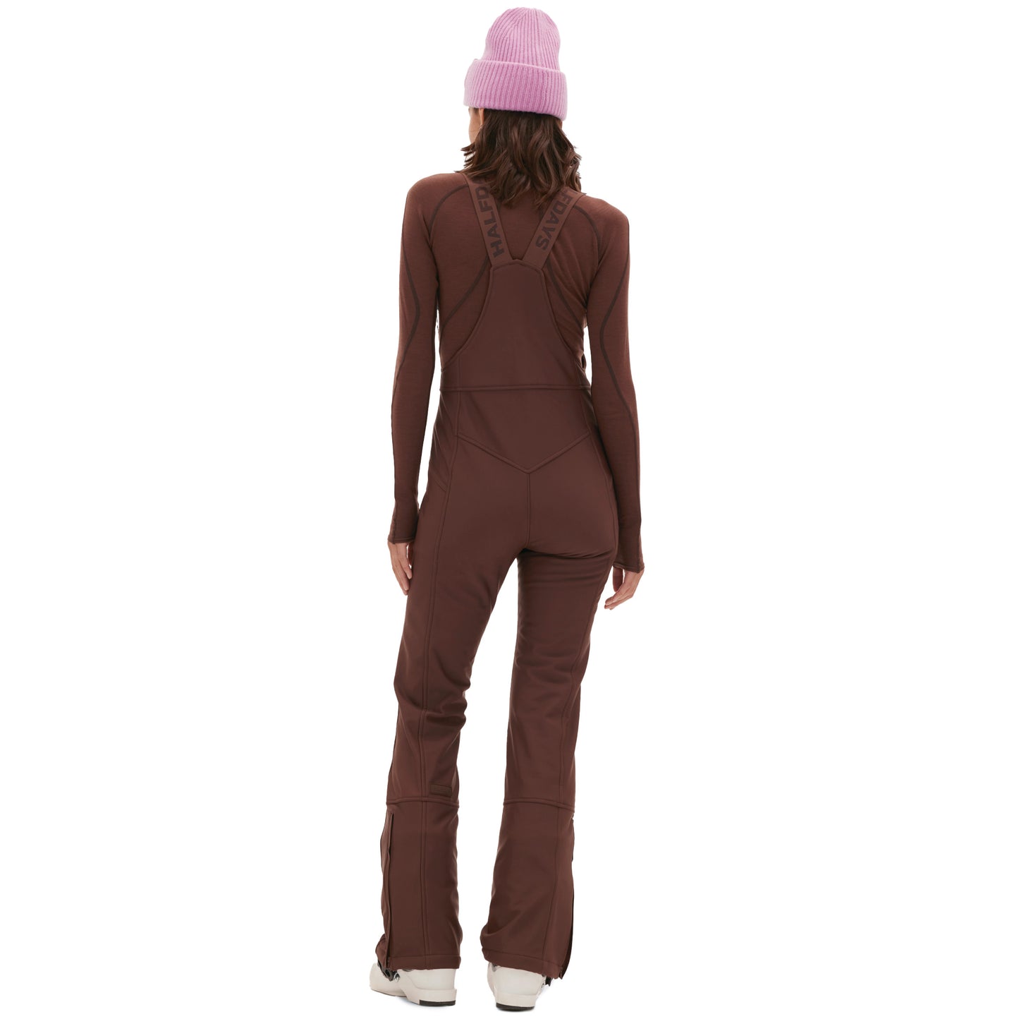 Woman in an Isabel Soft Shell Bib Pant by Halfdays, standing with her back to the camera, highlighting its sleek design and paired with a pink beanie.