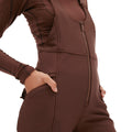 A person wears the Isabel Soft Shell Bib Pant by Halfdays, a brown, slim-fit piece with hands in pockets.