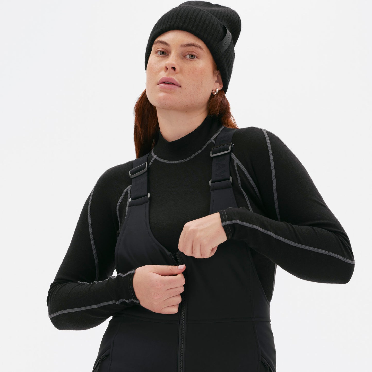 A person zips up the front of their slim-fit black Isabel Soft Shell Bib Pant from Halfdays, standing against a plain background.