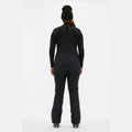 A person wearing Halfdays' Isabel Soft Shell Bib Pant in black slim-fit winter style and a beanie stands with their back to the camera against a white background, showcasing the sleek design of the gear.