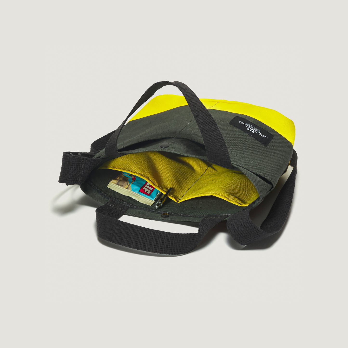 The New York Tote Small by Bags in Progress, Special Edition: Forest Green/Yellow, features a chic design with black handles. Inside, it includes a pocket for holding small plastic items and a blue wallet. Versatile and stylish, this tote is perfect for any occasion.