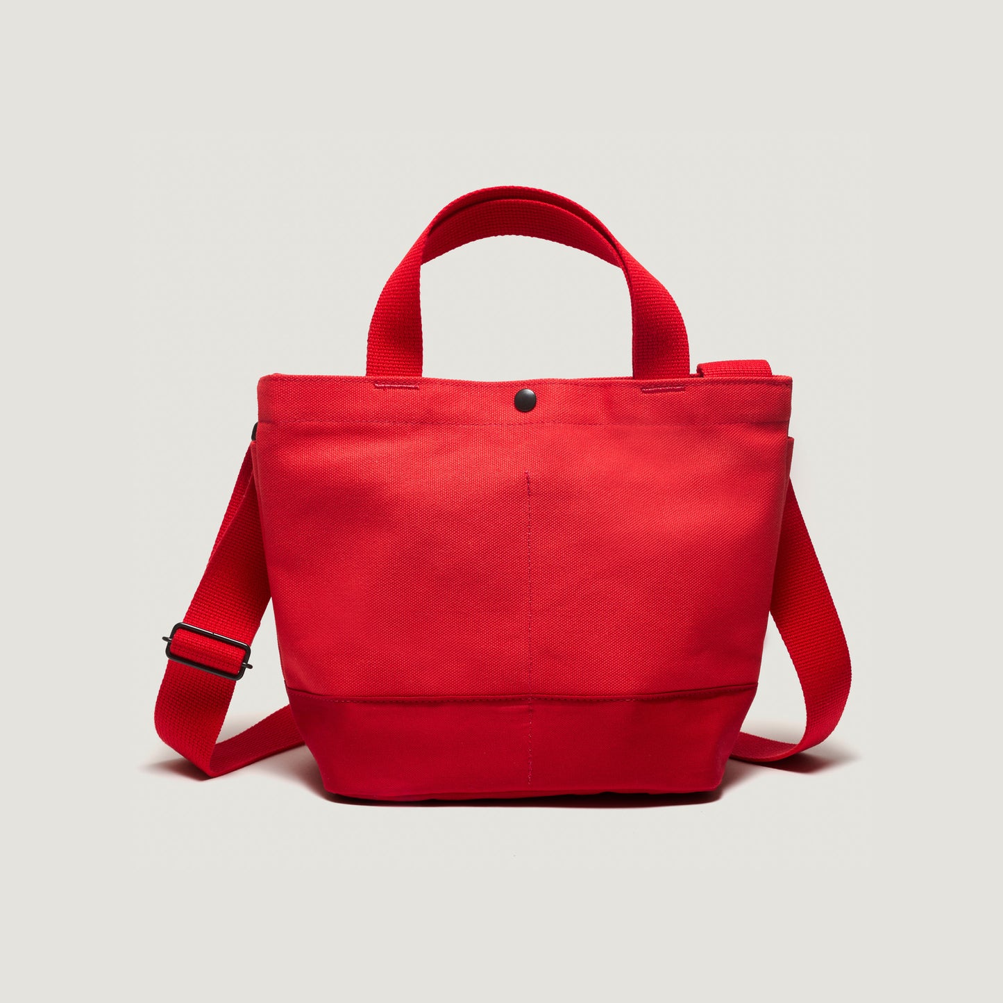 The New York Tote Small, Special Edition: Red/Red by Bags in Progress is a red canvas bag with two handles, an adjustable shoulder strap, and convenient pockets. It has a button closure and maintains a simple design.