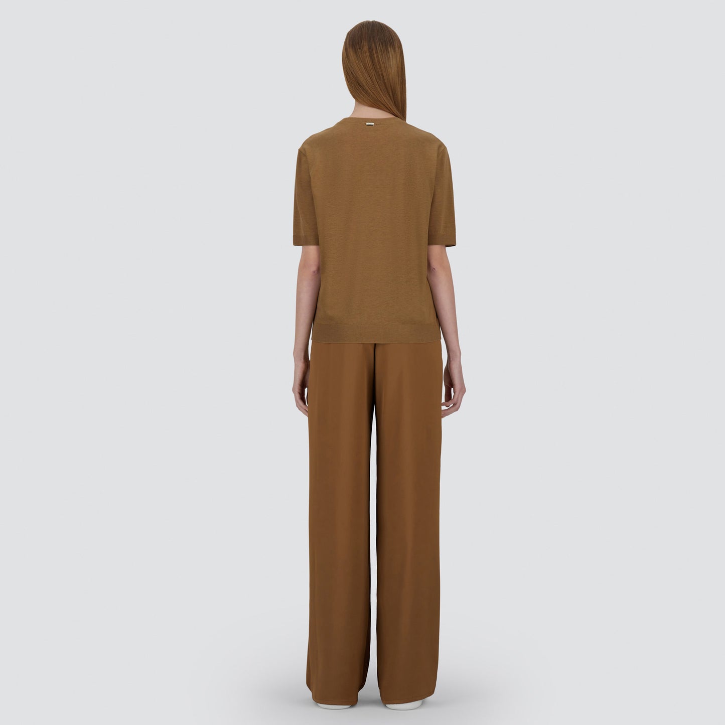A person faces away, wearing the Herno Satin Front T-Shirt with wide-leg brown pants against a plain light gray background.