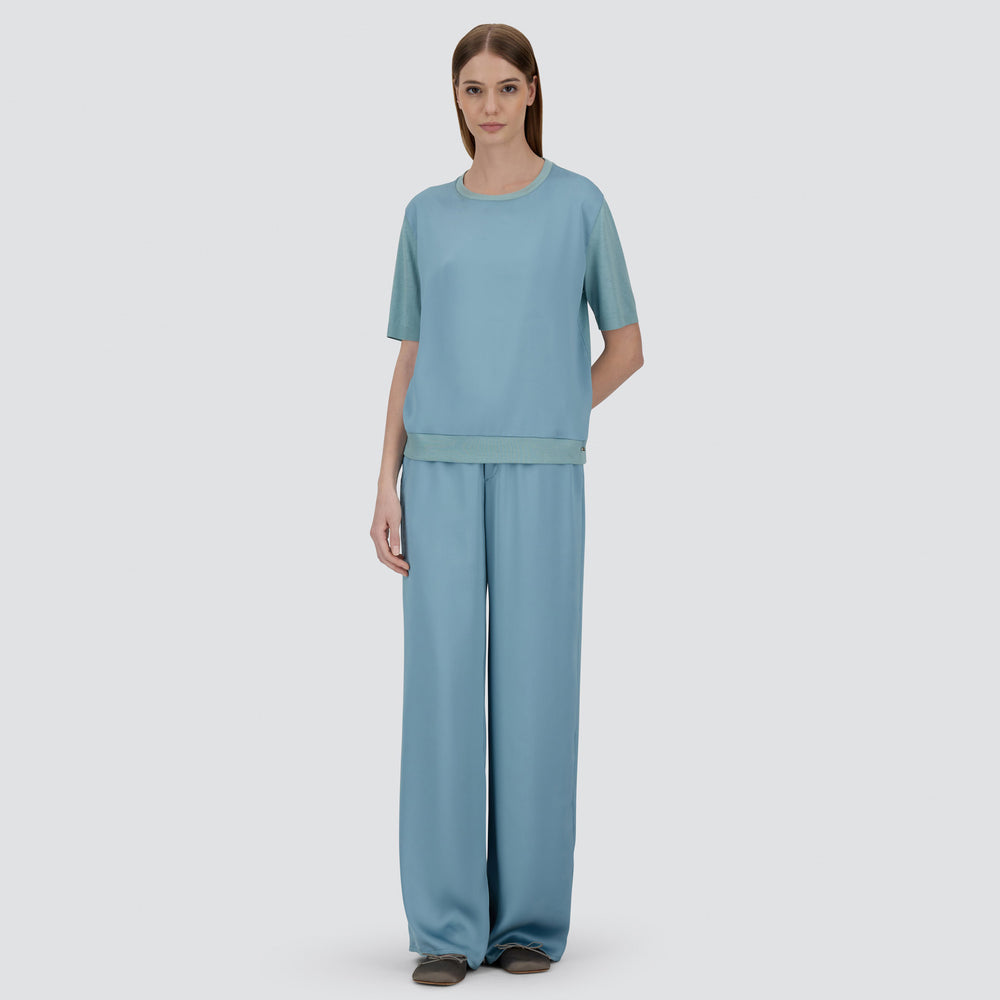 A woman faces forward in a loose-fitting Herno Satin Front T-Shirt and matching wide-leg pants with brown flats, set against a plain light background.
