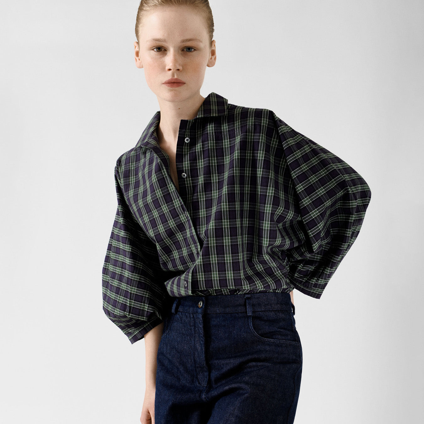 A person stands against a plain background wearing the Jan Machenhauer Nina Shirt in Purple Check, styled with high-waisted dark jeans.
