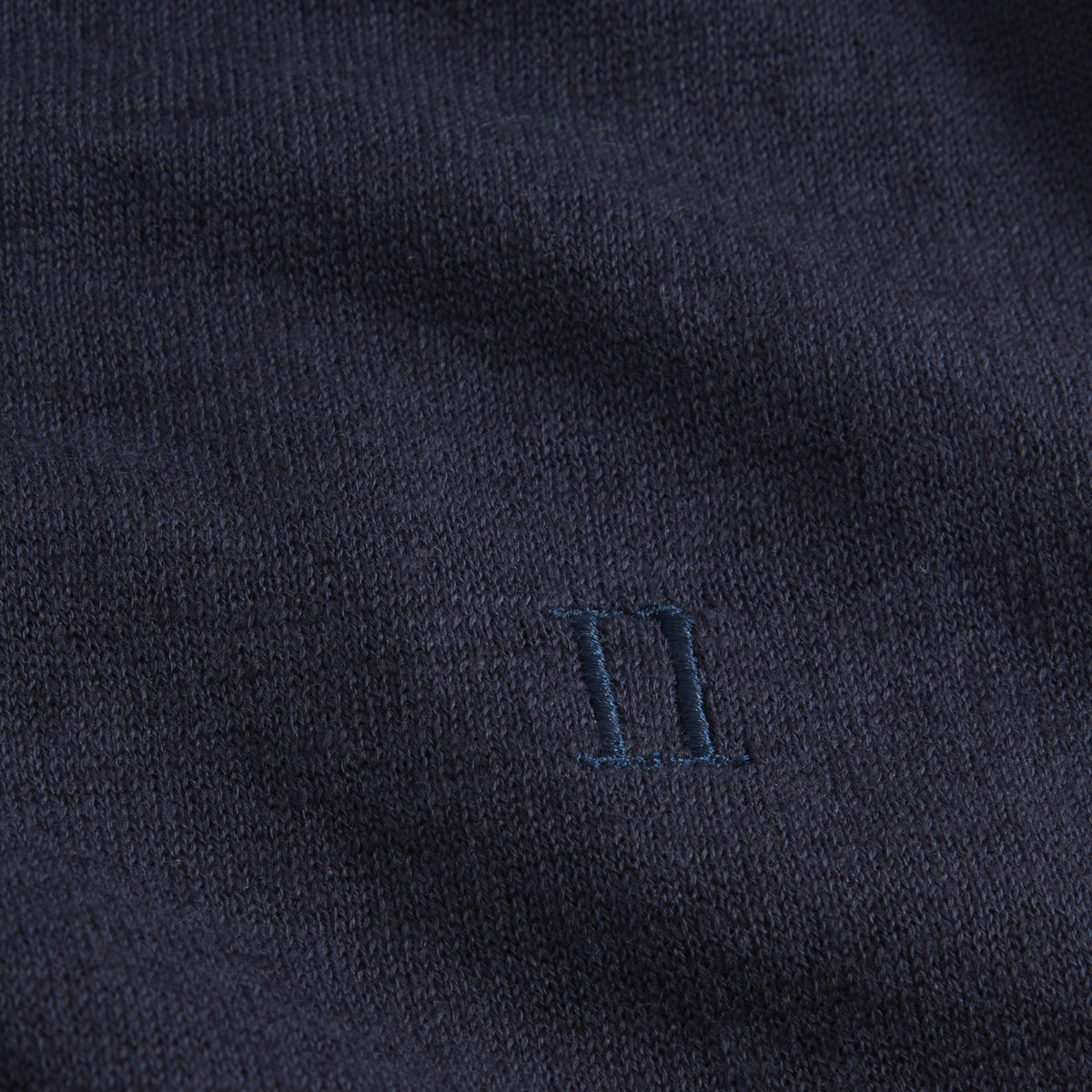Close-up of Les Deux Knit Polo in dark navy blue, featuring a knitted Roman numeral II and embroidered "Encore" in matching thread at the center for a vintage-inspired look.