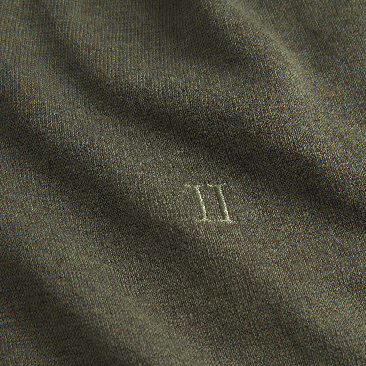 Close-up of olive green Les Deux Knit Polo, featuring the Roman numeral II delicately embroidered in lighter green thread for a subtle vintage touch.