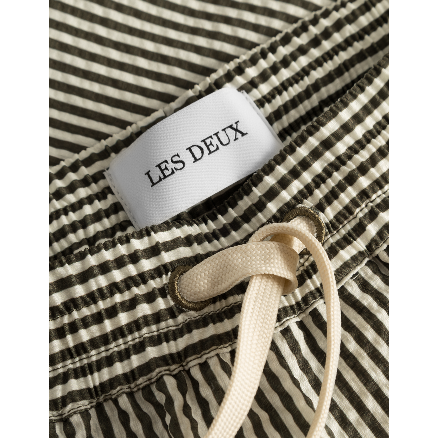 Close-up of Stan Stripe Seersucker Swim Shorts with a Les Deux label and beige drawstring waist.