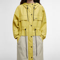 The person is wearing the Barbour Evie Showerproof Parka, a yellow and beige hooded jacket with black drawstrings and buttons, providing excellent weather protection.