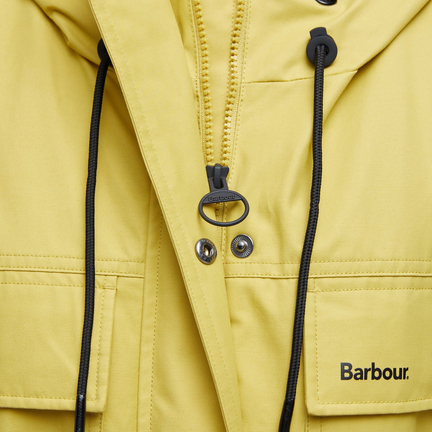Close-up of a yellow Evie Showerproof Parka by Barbour, featuring a zipper, snap buttons, drawstrings, and the Barbour logo on a front pocket. The weather-protective parka has an adjustable hood for added functionality.