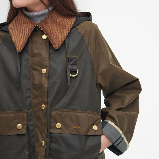 A woman dressed in a Barbour Reighton Spey Waxed Jacket with an oversized cord collar stands against a plain background. The visible parts include her torso and part of her head. The jacket, enhanced with gold buttons and large pockets, also boasts subtle tartan trims.