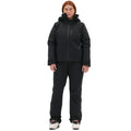 Against a white backdrop, a woman stands confidently in her ski boots, clad in the Lawrence Jacket by Halfdays and black winter pants.