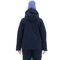 A woman in the Lawrence Jacket by Halfdays and a blue beanie stands with her back to the camera against a pristine white backdrop, conveying calm readiness for the slopes.