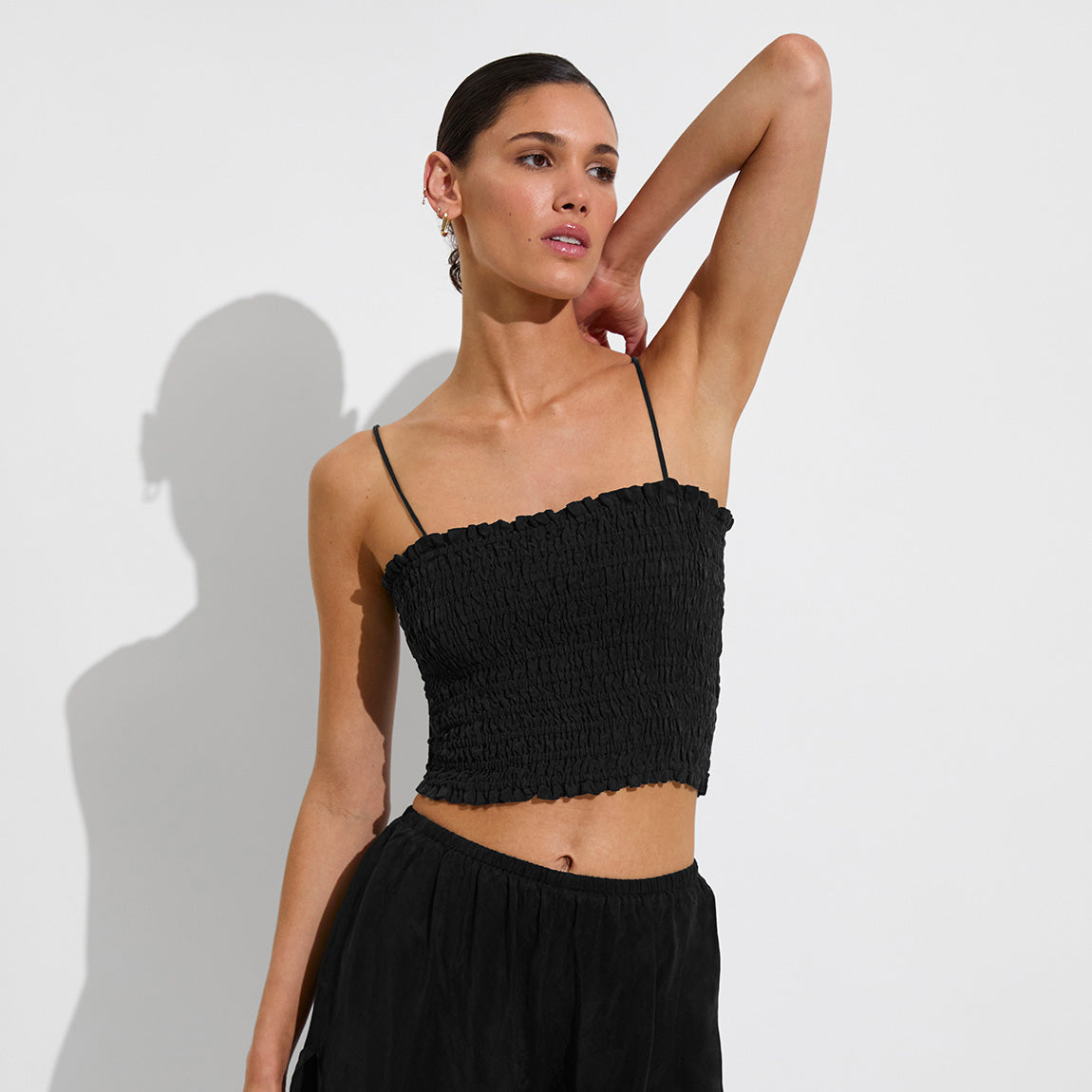 A woman wears the Left On Friday Cabana Top in black with adjustable straps and matching pants, posing against a plain white background with one arm raised behind her head.