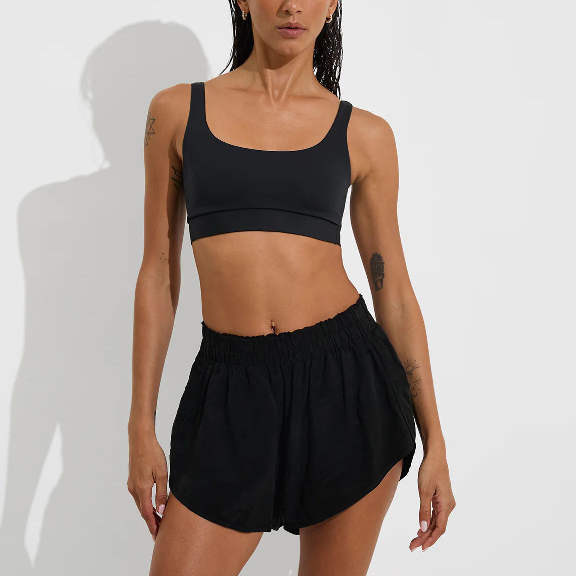 A person wearing Left On Friday's black Day Trip Short and a black sports bra stands against a plain white background.