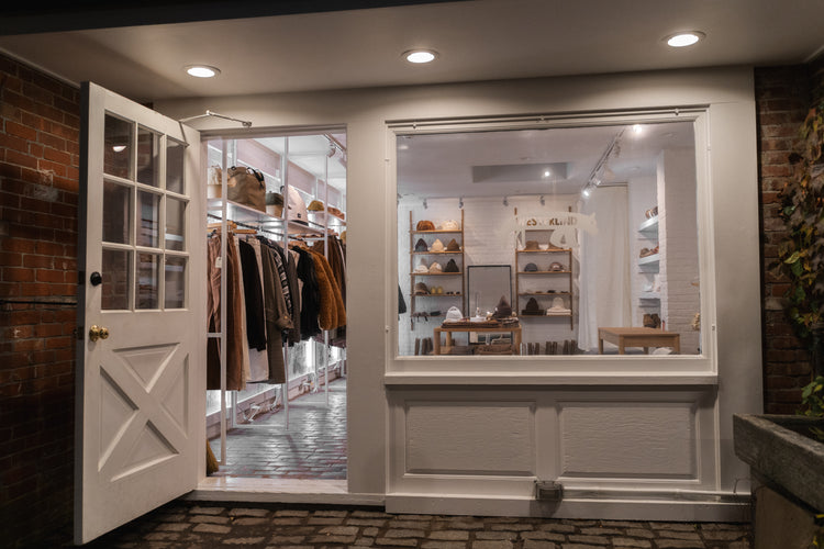 Store interior with open white door revealing clothing racks and shelves.