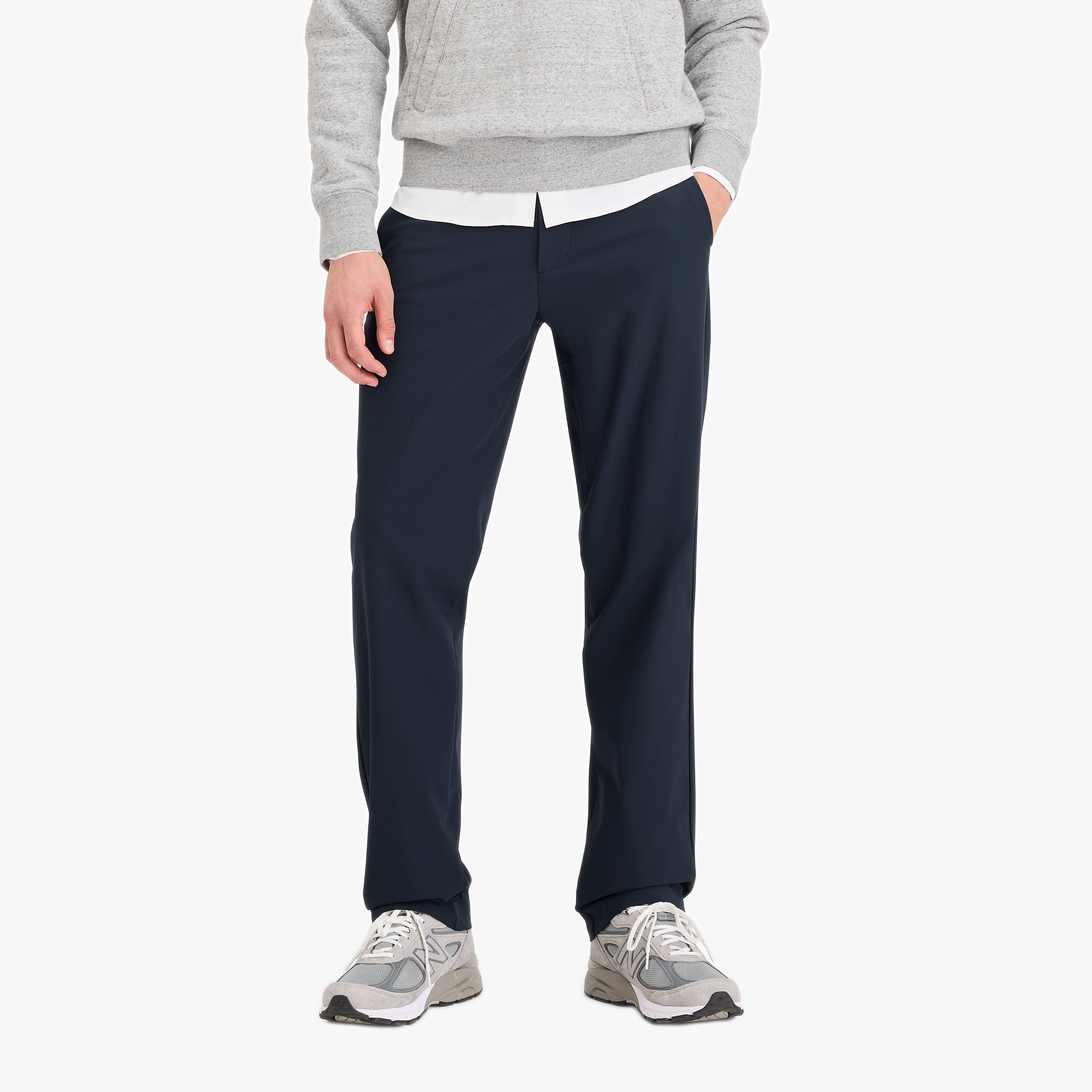 A person wearing a light gray sweatshirt, white shirt, Dockers Go Airweave Chino Str in Navy Blazer, and gray sneakers stands with one hand in their pocket against a plain white background.