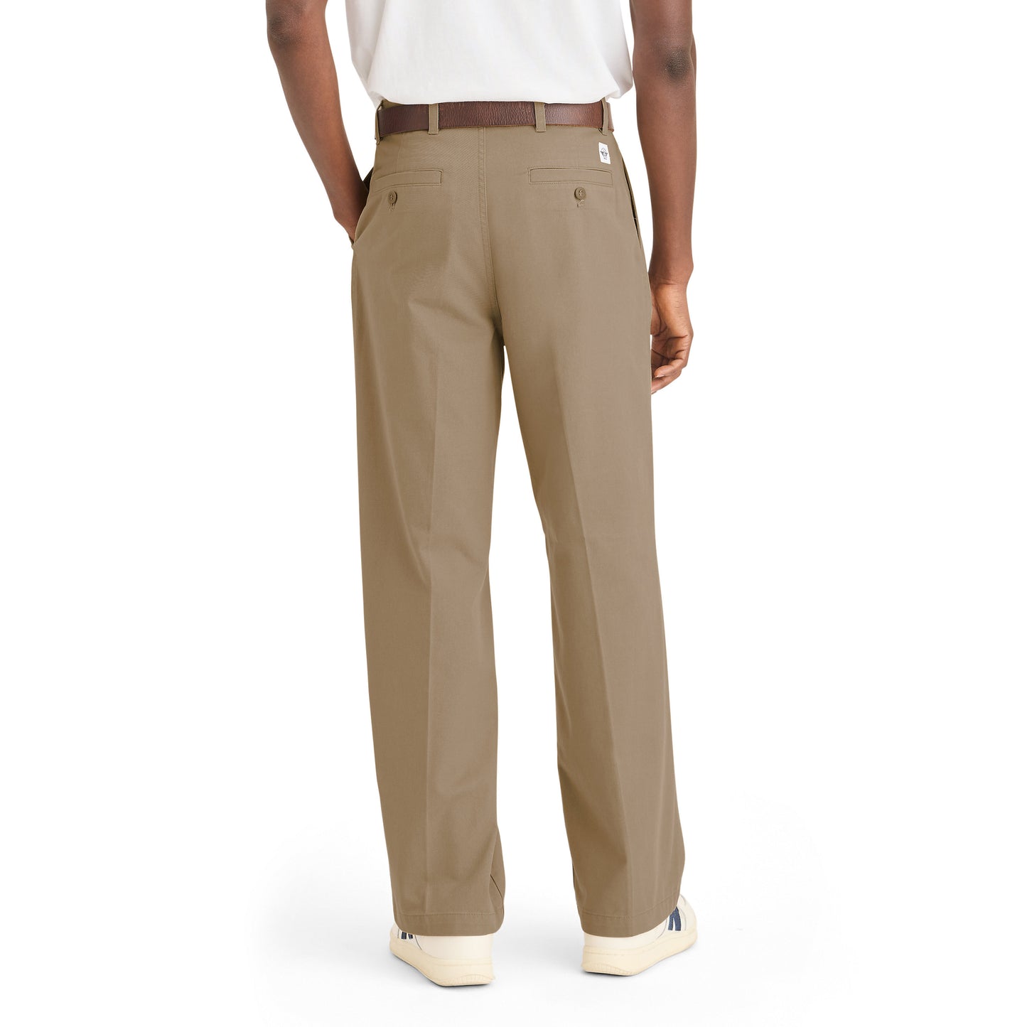 A person is shown from the back wearing Dockers Genderless 86 Original Pleated Chino in khaki with a brown belt, white sneakers, and a white shirt, set against a plain white background.