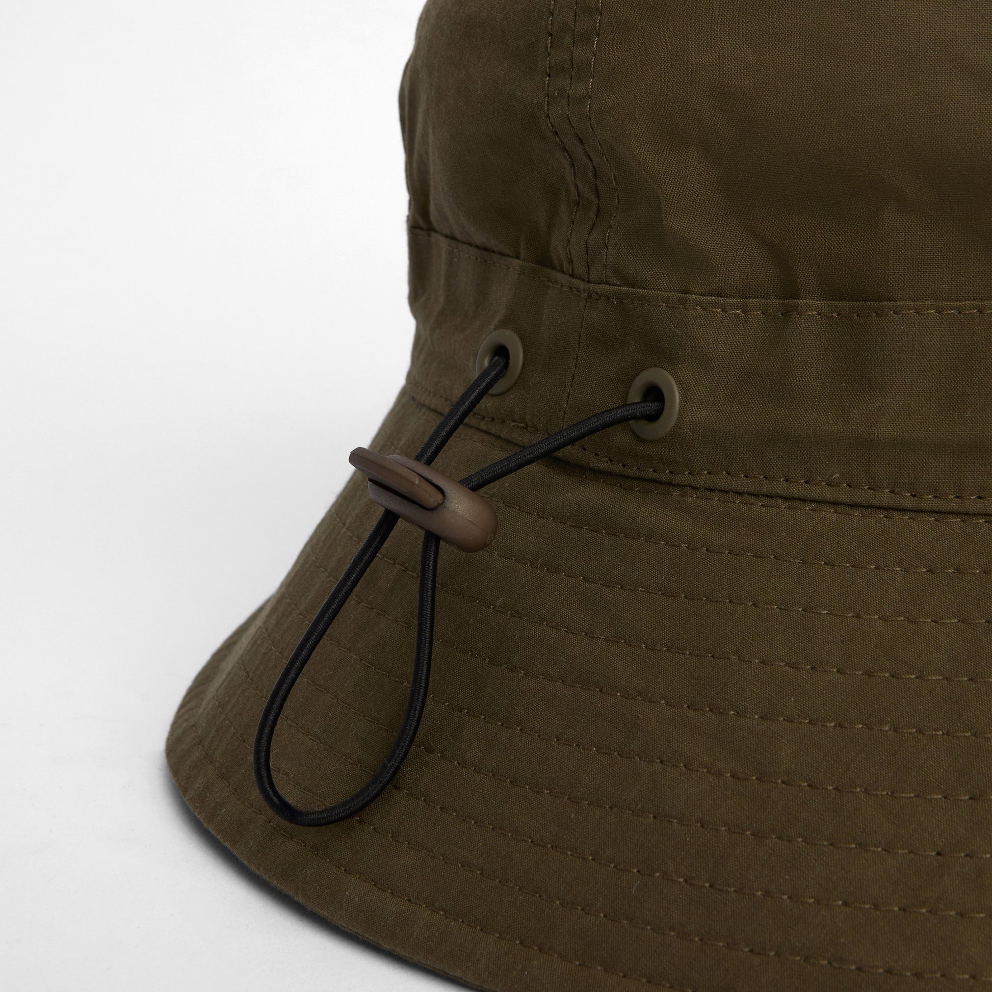 Close-up of the Barbour Transport 6 Panel Bucket Hat in olive green, featuring a black adjustable drawstring with a plastic toggle.