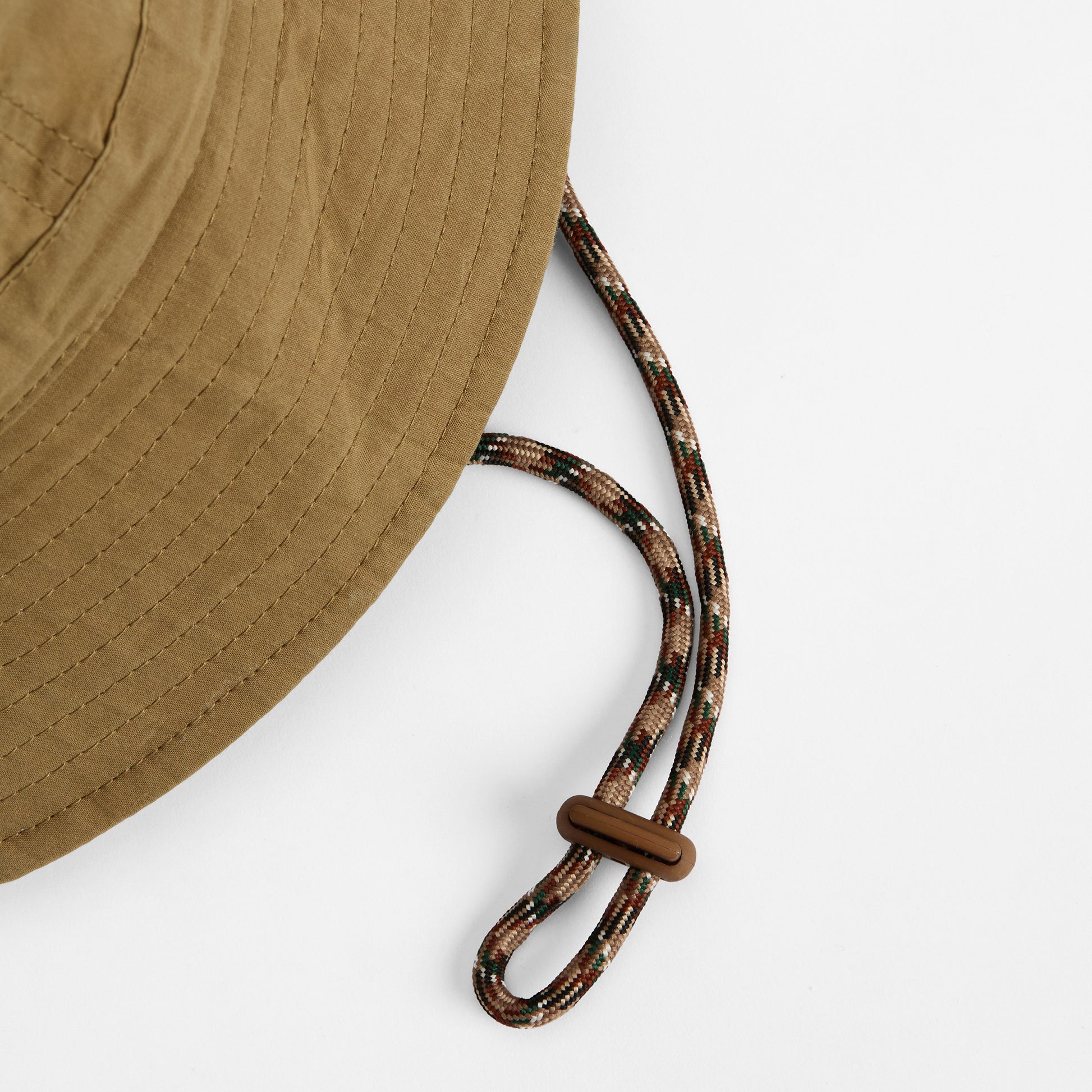 Close-up of the Barbour Transport 6 Panel Bucket Hat in brown, featuring a patterned adjustable chin cord with a plastic toggle, set against a white background.