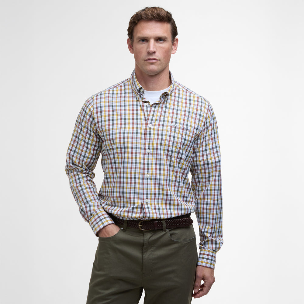 A person stands against a plain background, dressed in a vibrant Barbour Hallhill Performance Shirt and green pants with a timeless check design, maintaining a neutral expression.