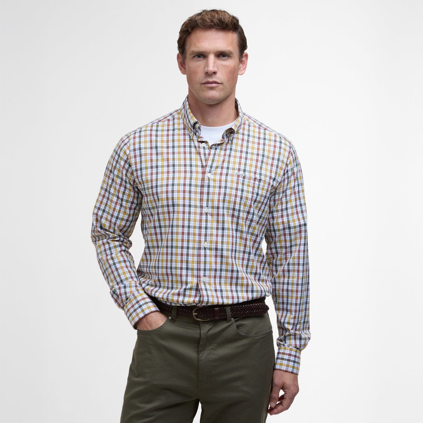 A person stands against a plain background, dressed in a vibrant Barbour Hallhill Performance Shirt and green pants with a timeless check design, maintaining a neutral expression.