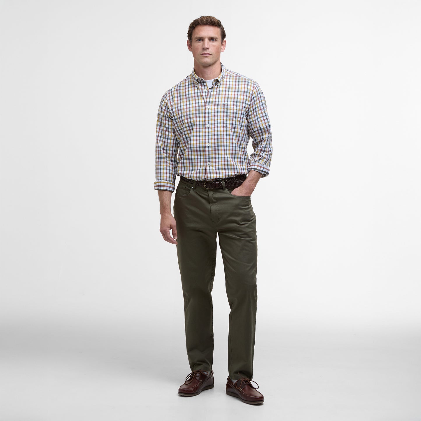 A man stands against a plain background, showcasing a Barbour Hallhill Performance Shirt with a classic check design, paired with khaki pants and brown shoes.