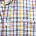 Close-up of the Barbour Hallhill Performance Shirt featuring a classic check pattern in white, yellow, orange, and gray. The chest pocket displays the iconic "Barbour" label in green.