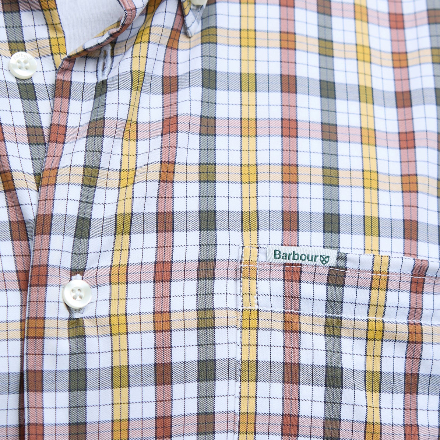 Close-up of the Barbour Hallhill Performance Shirt featuring a classic check pattern in white, yellow, orange, and gray. The chest pocket displays the iconic "Barbour" label in green.