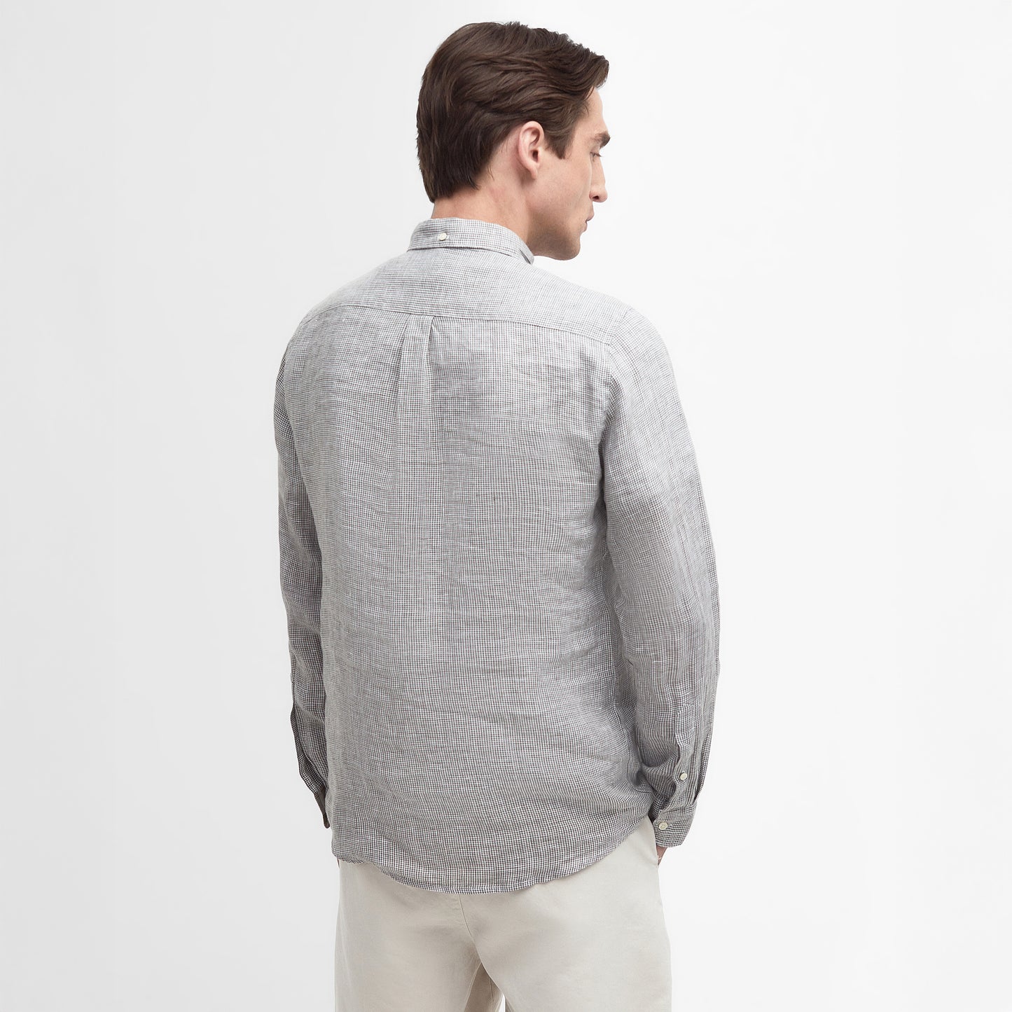 A man models the Barbour Linton Tailored Shirt in light gray, paired with beige pants, standing and facing away against a plain white background.