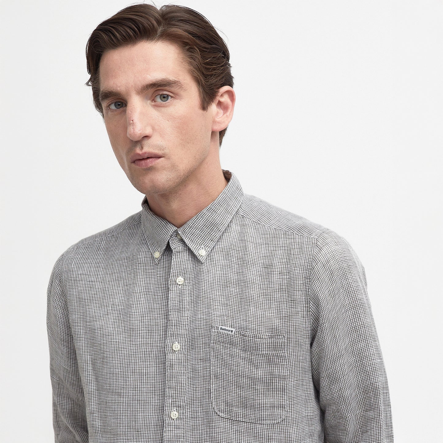 A man wearing the Barbour Linton Tailored Shirt, a gray shirt with a micro houndstooth weave, stands against a plain white background looking slightly to the side.