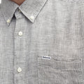 Close-up of a person wearing the Barbour Linton Tailored Shirt, featuring a gray and white micro houndstooth weave, button-up front, chest pocket, and a small "Barbour" logo tag on the pocket.