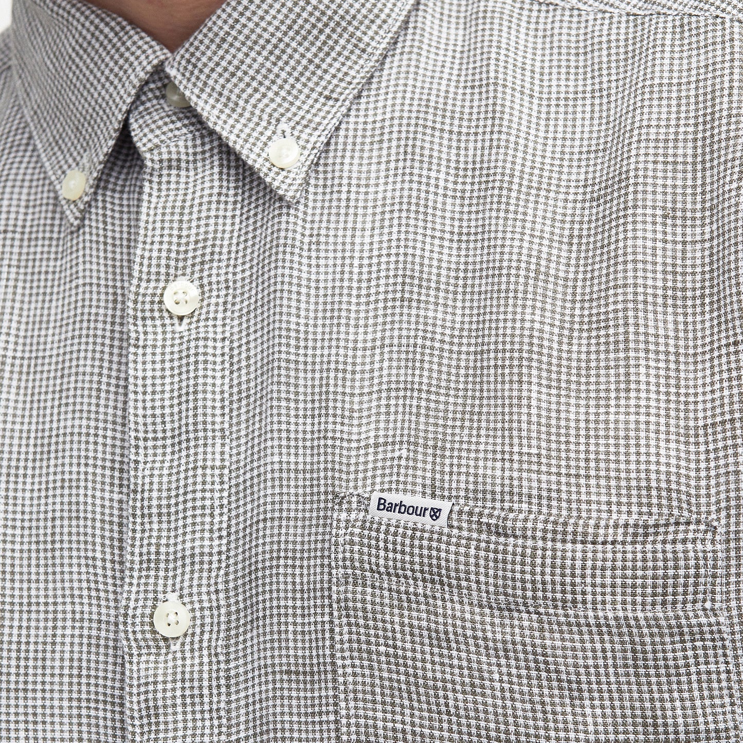 Close-up of a person wearing the Barbour Linton Tailored Shirt, featuring a gray and white micro houndstooth weave, button-up front, chest pocket, and a small "Barbour" logo tag on the pocket.