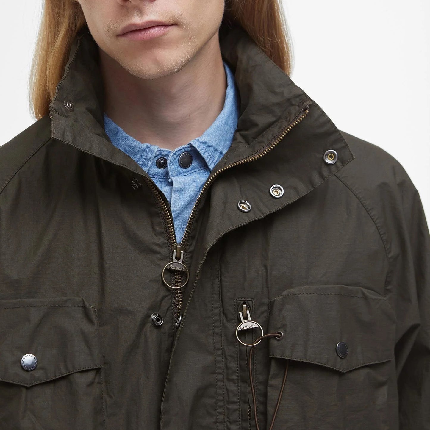 A person in a green Barbour Westmorland Showerproof Jacket over a blue shirt exudes countryside charm, featuring functional details like a sturdy zipper and classic buttons.