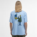 A person with long blonde hair is wearing Barbour's Newclyde Graphic T-Shirt in light blue, showcasing an archive-inspired design with a cartoon character holding a bird on the back.
