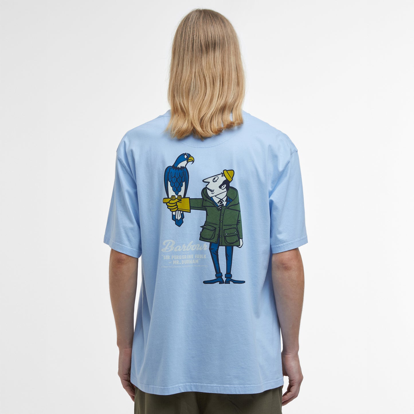 A person with long blonde hair is wearing Barbour's Newclyde Graphic T-Shirt in light blue, showcasing an archive-inspired design with a cartoon character holding a bird on the back.